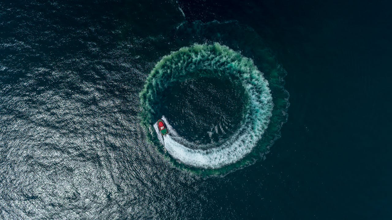 A speedboat creates a circular wave pattern on the open sea, captured from a high aerial perspective.