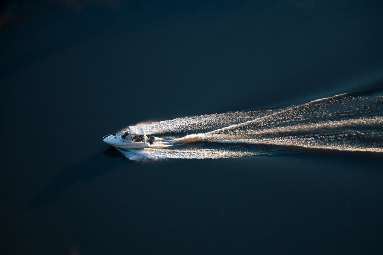 Aerial shot of a speedboat cruising on a calm open water surface, leaving a trail.